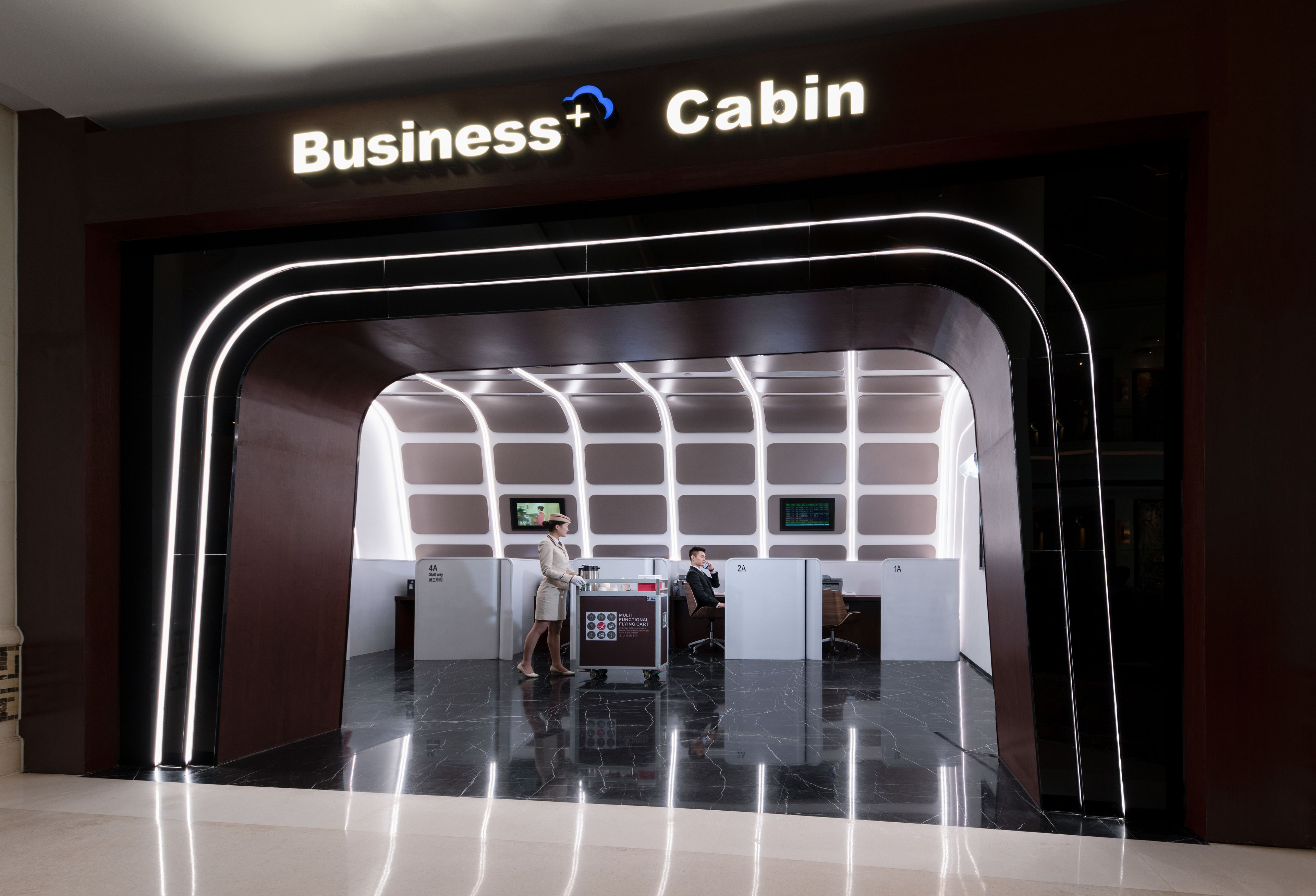 A Business+ Cabin entrance with a modern design, including a digital display and a reception area.