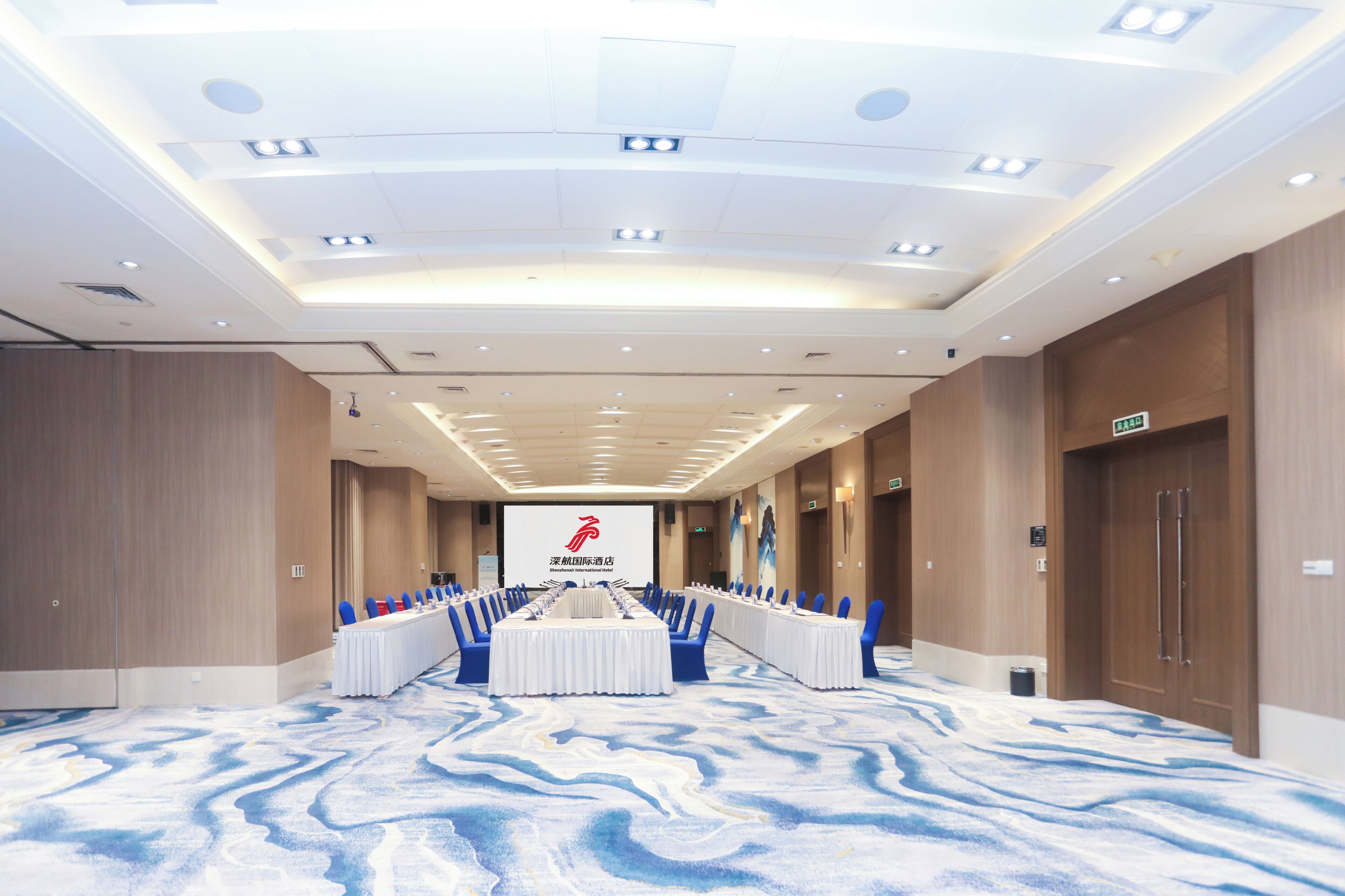 Una sala de conferencias con una larga mesa, sillas azules y piso alfombrado.
