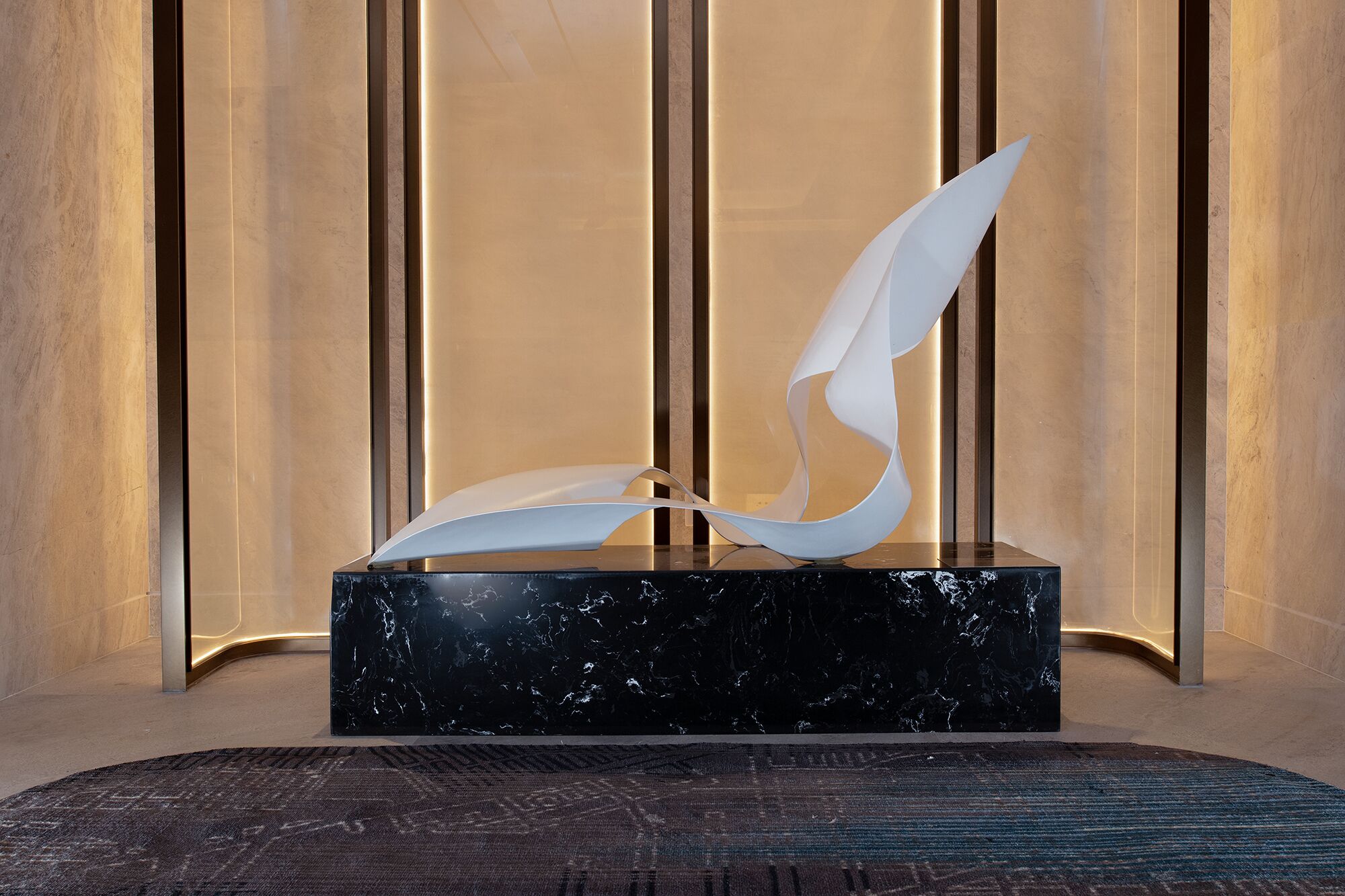 A modern sculpture on a marble base in a well-lit room with vertical paneling.