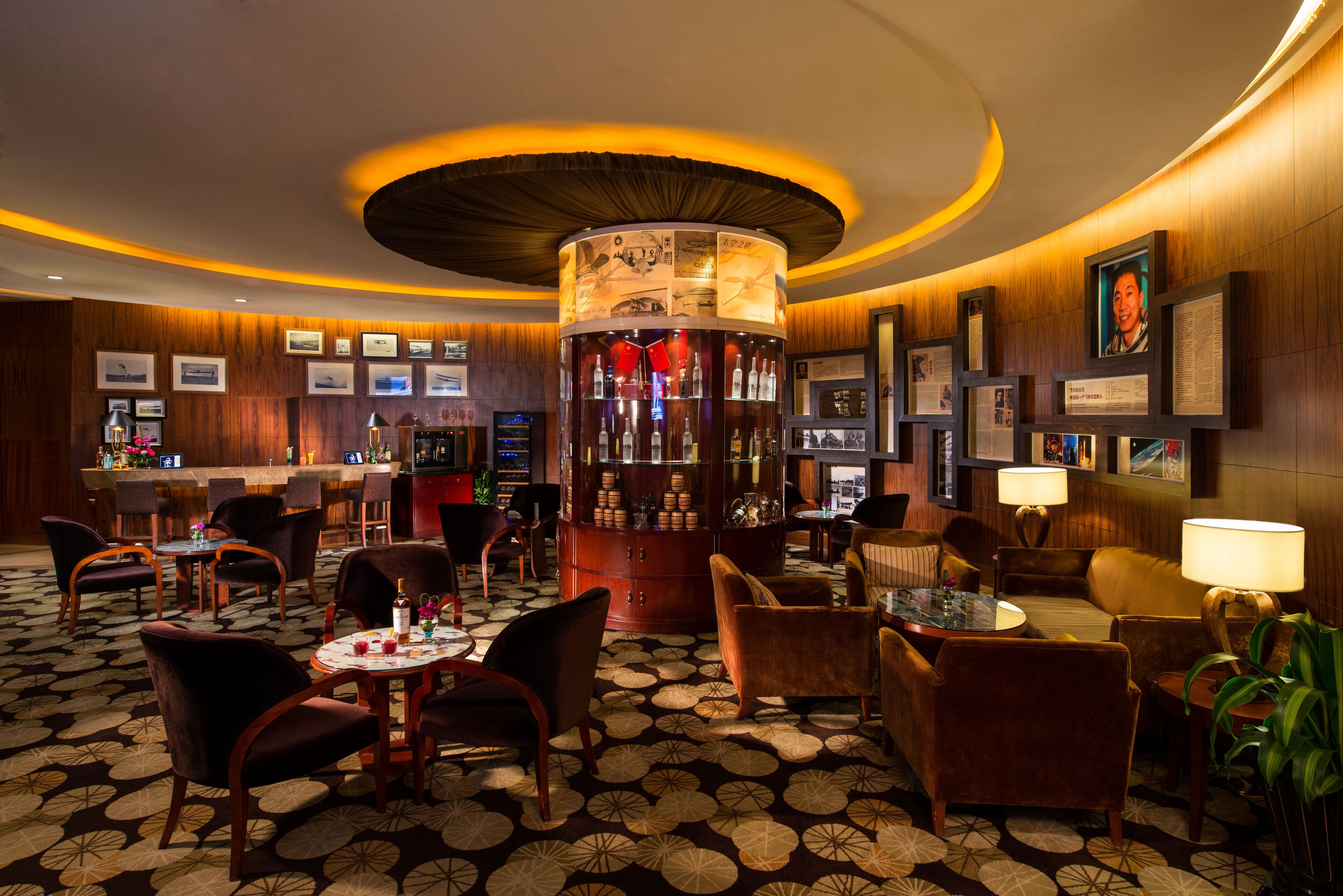 A bar area with a circular bar counter, framed pictures on the walls, and a patterned carpet.