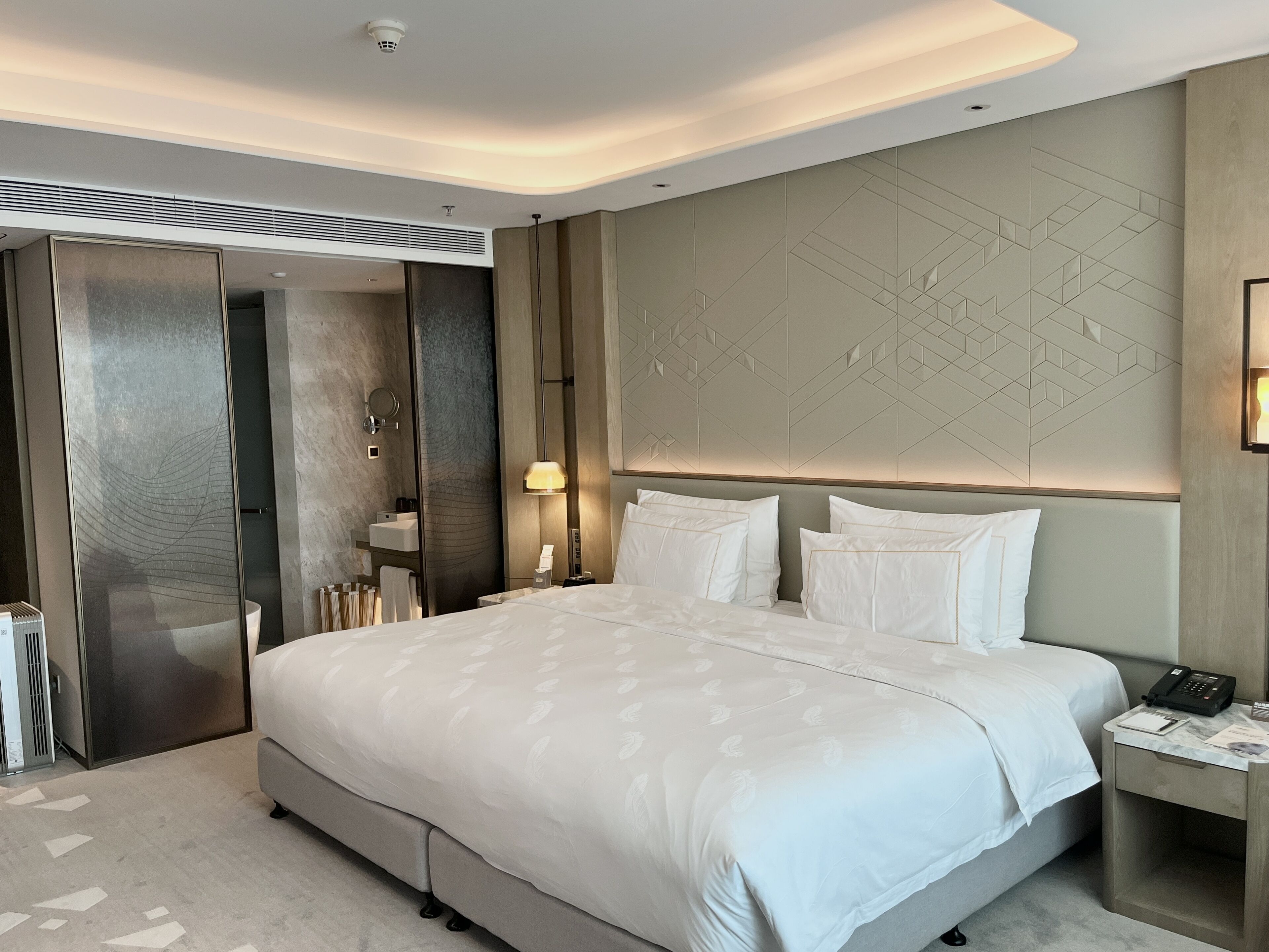 Una habitación de hotel moderna con una cama grande, una mesita de noche con lámpara, un armario empotrado y un diseño geométrico en la pared.