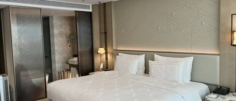 Una habitación de hotel moderna con una cama grande, una mesita de noche con lámpara, un armario empotrado y un diseño geométrico en la pared.