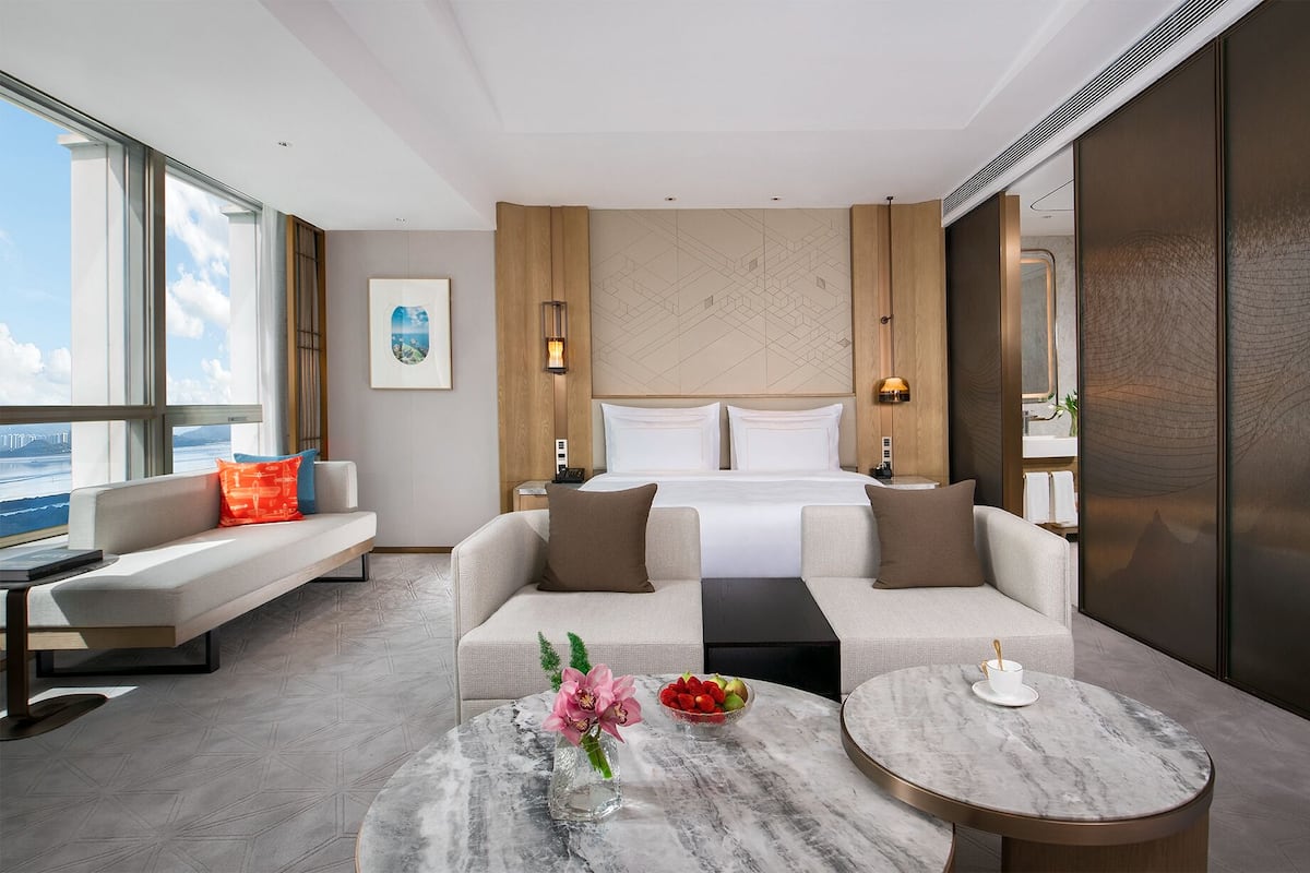 Une chambre d’hôtel moderne équipée d’un lit, de deux canapés, d’une table basse et d’une grande fenêtre donnant sur un beau paysage.