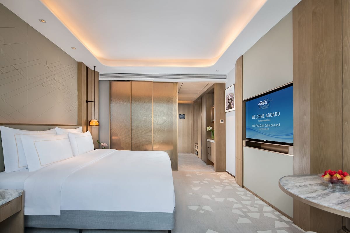 Une chambre d’hôtel moderne avec un grand lit, une télévision et une petite table sur laquelle sont disposés des fruits.