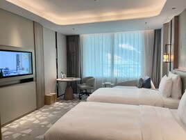 A hotel room with two beds, a TV, a small table, and a chair.