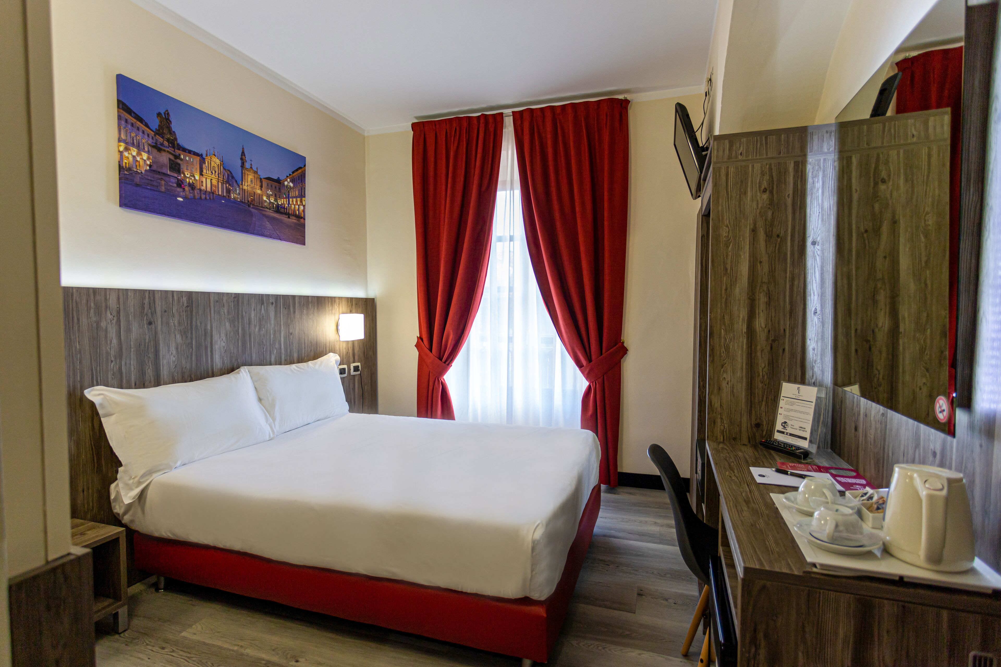 A hotel room with a bed, a desk with a laptop, and a painting on the wall.