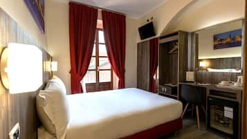 A hotel room with a bed, desk, and a TV mounted on the wall.