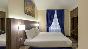 Una habitación de hotel con una cama grande, cabecera de madera, una mesita de noche, una lámpara de pared, un cuadro y una ventana con cortinas azules.