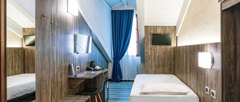 A compact, well-lit room with a bed, a desk, and a chair.