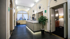 A hotel lobby with a reception desk, a clock, and an elevator. - Hotel Urbani (Turin)