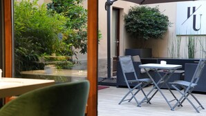 An outdoor seating area with tables and chairs, surrounded by plants and a large wall with a letter 'U'. - Hotel Urbani (Turin)