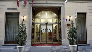 A hotel entrance with a glass door, flags, and potted plants. - Hotel Urbani (Turin)