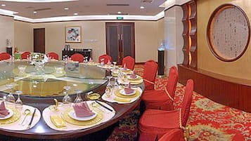 A hotel lobby with a round dining table, red upholstered sofas, and a patterned carpet.