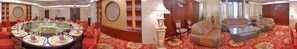 A hotel lobby with a round dining table, red upholstered sofas, and a patterned carpet.