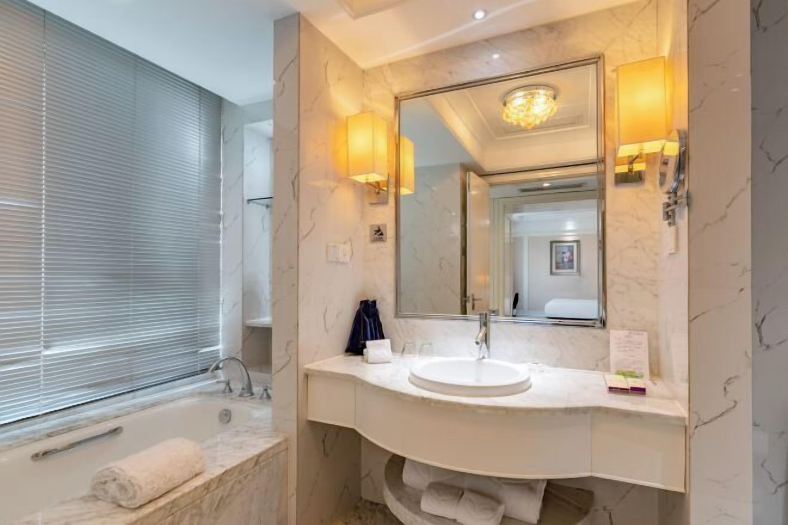 Un baño moderno con lavamanos de mármol, un espejo grande y una bañera.