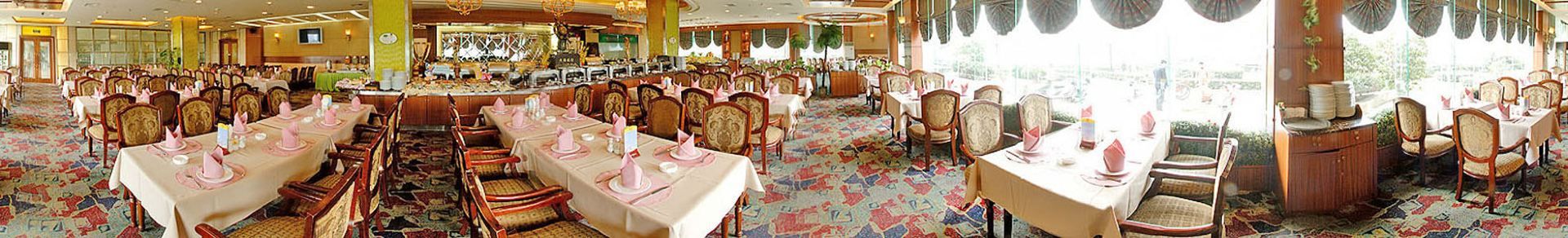 A banquet hall with multiple round tables, each set with white tablecloths and pink napkins.