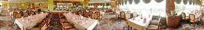 Un salón de banquetes con varias mesas redondas, cada una con manteles blancos y servilletas rosas.