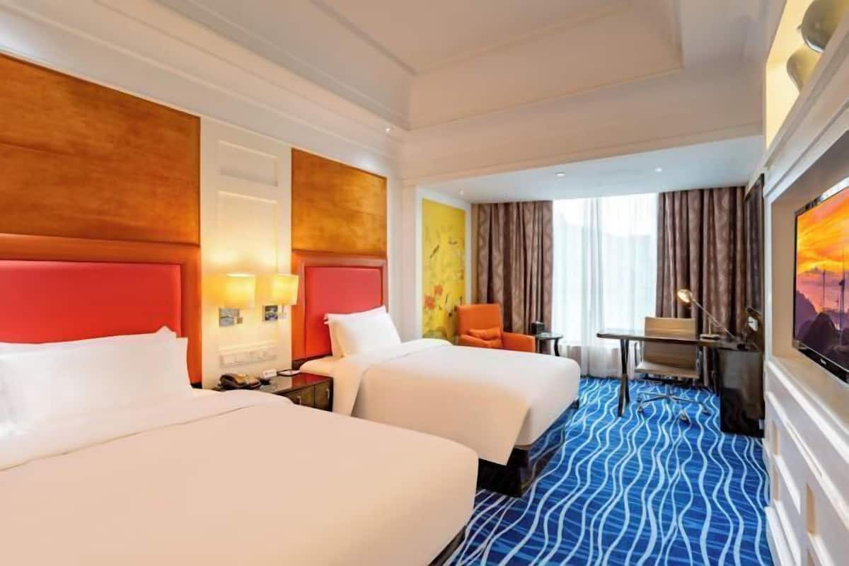A hotel room with two beds, a desk, a chair, and a TV.