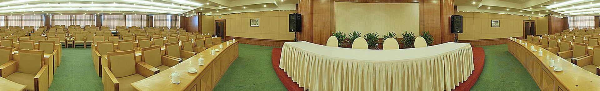Une salle de conférence avec des rangées de chaises, une longue table recouverte d’une nappe et une estrade avec un pupitre.