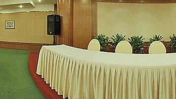 Une salle de conférence avec des rangées de chaises, une longue table recouverte d’une nappe et une estrade avec un pupitre.