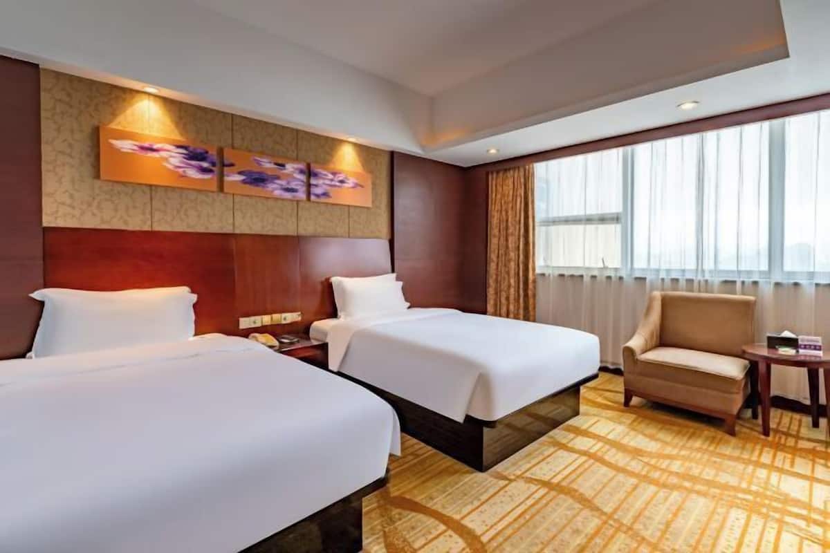 A hotel room with two beds, a sofa, a small table, and a large window with curtains.