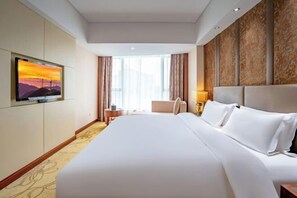 A hotel room with a large bed, a television on the wall, a window with curtains, and a patterned wall.