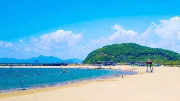 A beach with a lifeguard tower, clear blue sky, and a hill in the background.