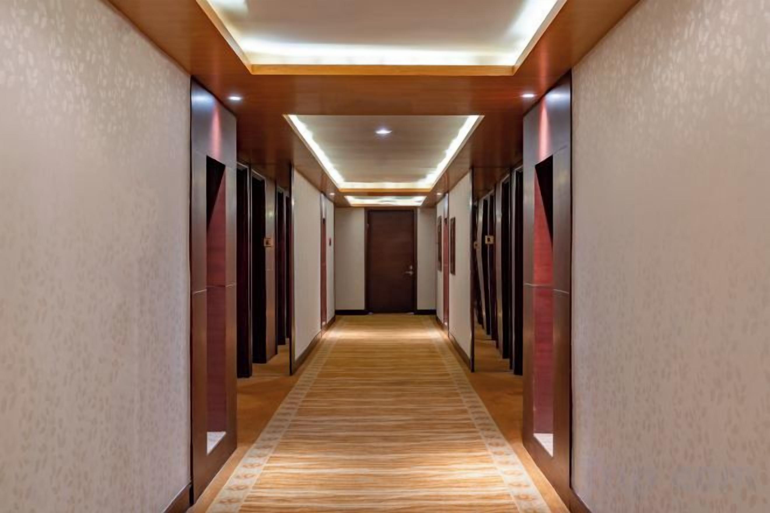 Pasillo de hotel con piso alfombrado, puertas a ambos lados y techo con iluminación empotrada.