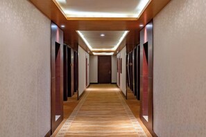 A hotel hallway with a carpeted floor, doors on both sides, and a ceiling with recessed lighting.
