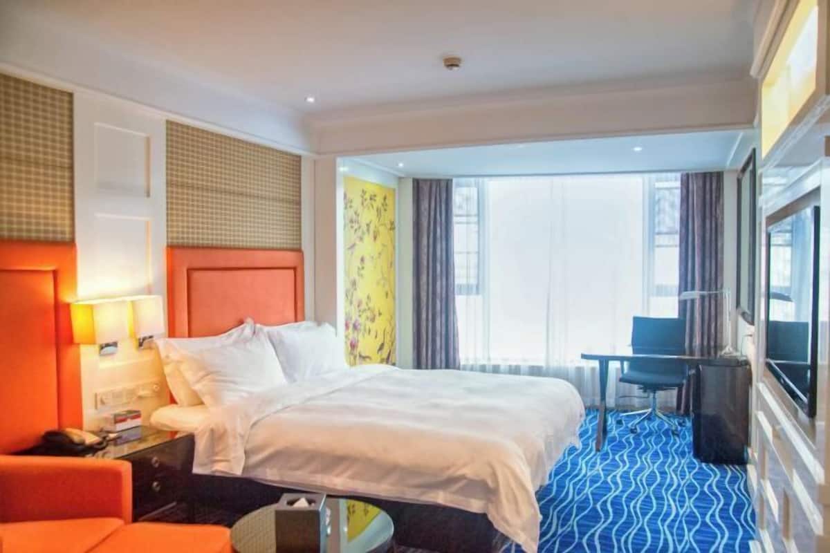 A hotel room with a bed, a desk, a chair, a TV, and a window with curtains.