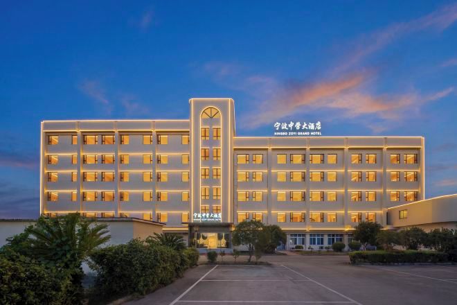 Hotel de varios pisos con entrada central y estacionamiento al frente.