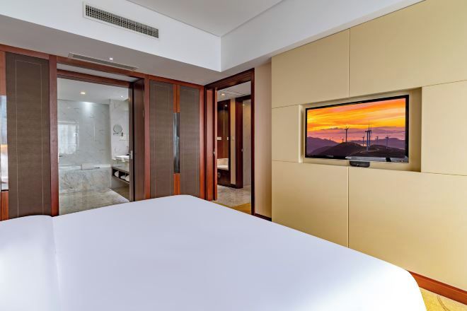 Habitación de hotel con una cama grande, un televisor montado en la pared y una puerta corredera que da al baño.