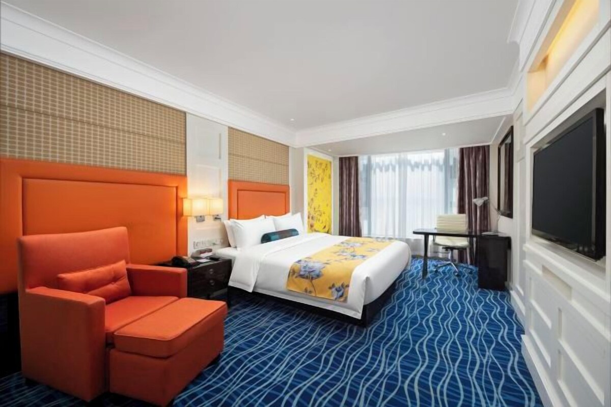 A hotel room with a bed, a chair, a desk, and a television.