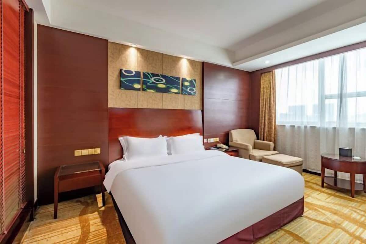 A hotel room with a large bed, a small table, a chair, and a decorative wall panel.