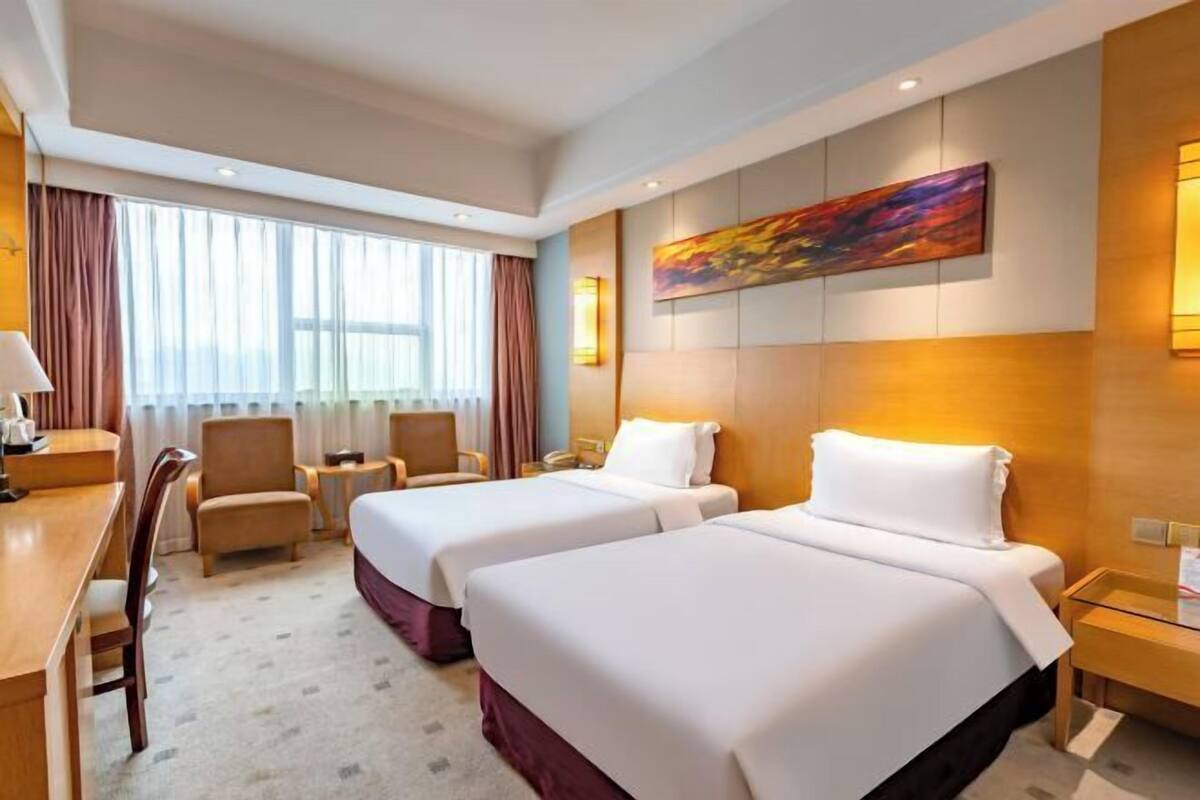A hotel room with two beds, a desk, a chair, and a large window with curtains.