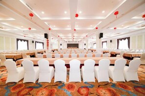 Un salón de conferencias con filas de mesas y sillas, piso alfombrado y faroles rojos en el techo.