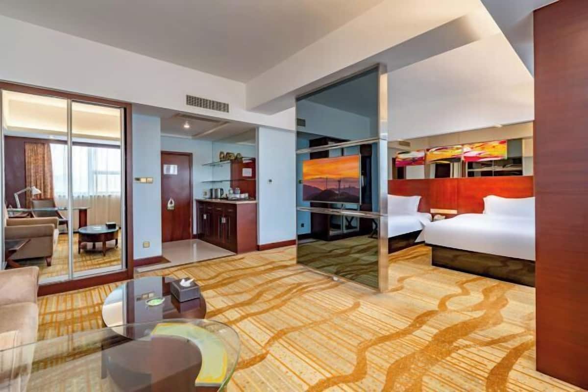 A hotel room with a bed, a glass table, a sofa, a desk, and a view of the cityscape.
