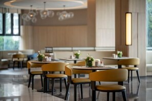 Un espace de restauration moderne avec des tables rondes et des chaises jaunes, de grandes fenêtres et un design épuré et minimaliste.