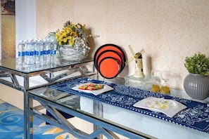 Une table en verre avec un set de table bleu, un vase avec des fleurs jaunes, une assiette noire et rouge, et une petite plante en pot.