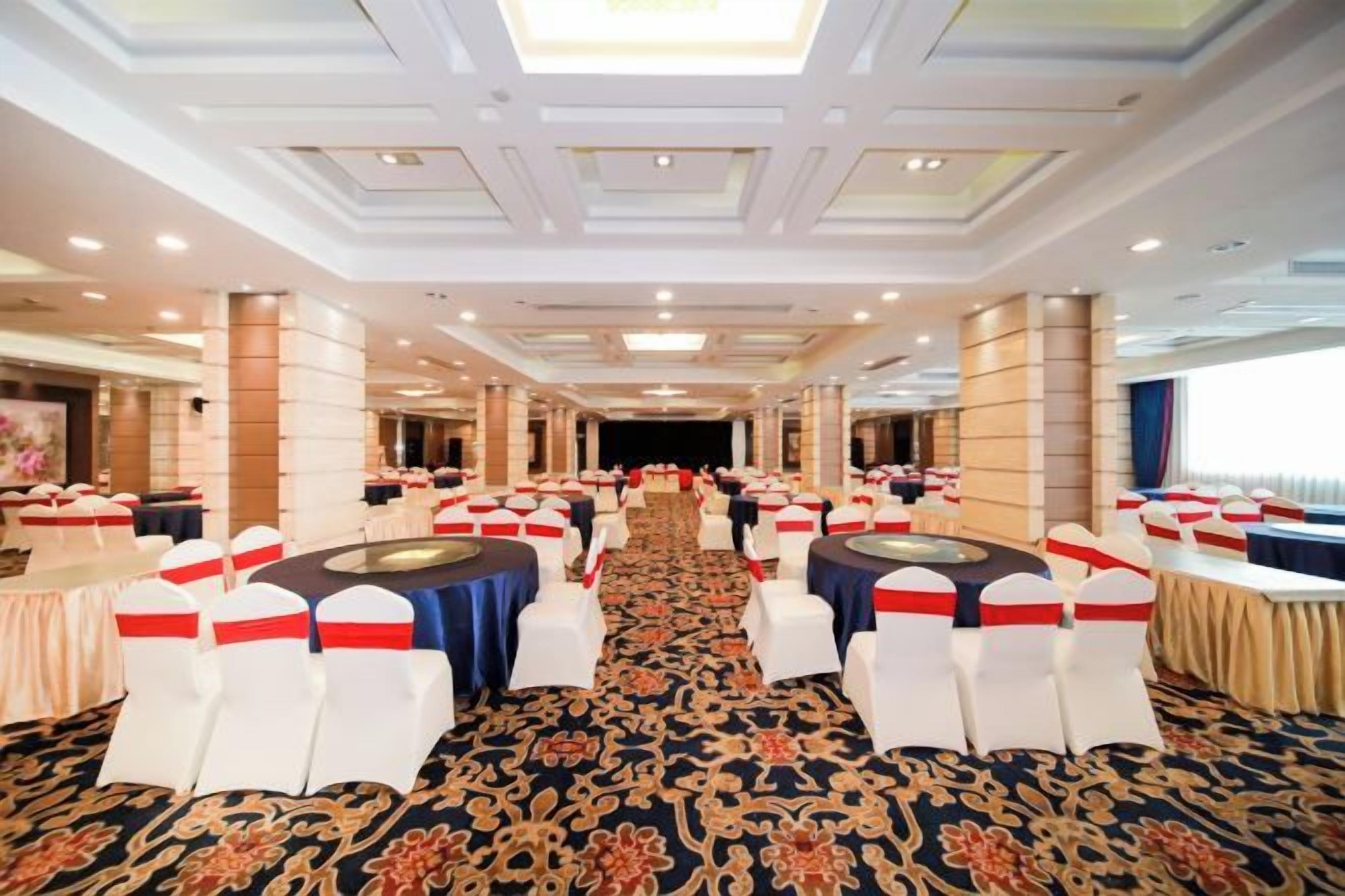 Un salón de banquetes con mesas redondas, sillas blancas y piso alfombrado.