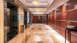 A hotel lobby with marble flooring, a reception desk, and a wall-mounted sign.