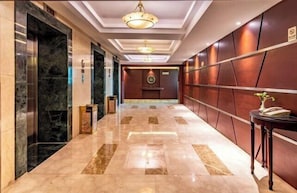 A hotel lobby with marble flooring, a reception desk, and a wall-mounted sign.
