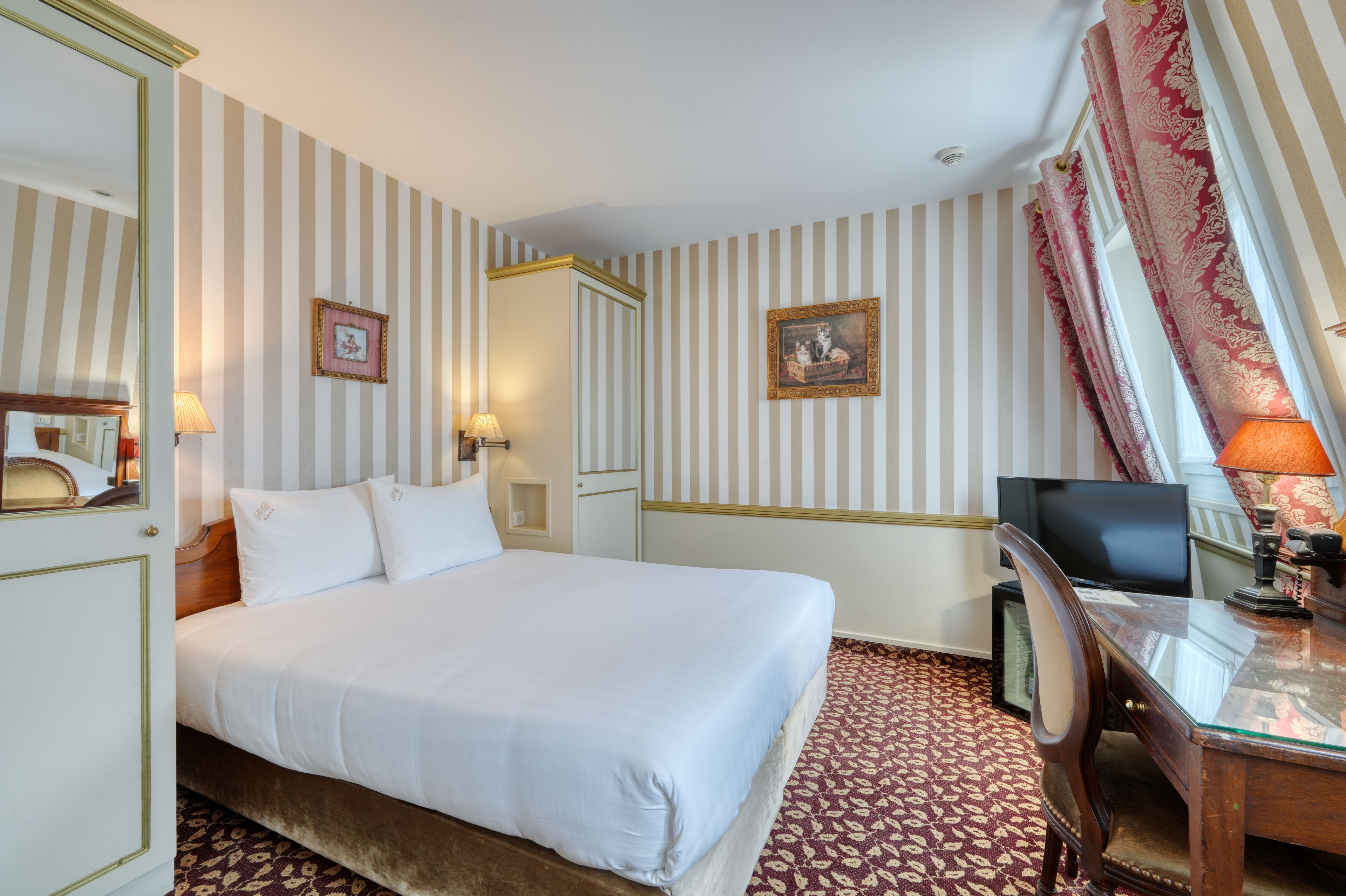 Une chambre d’hôtel avec un grand lit, un bureau avec une chaise, une télévision et un papier peint à rayures.