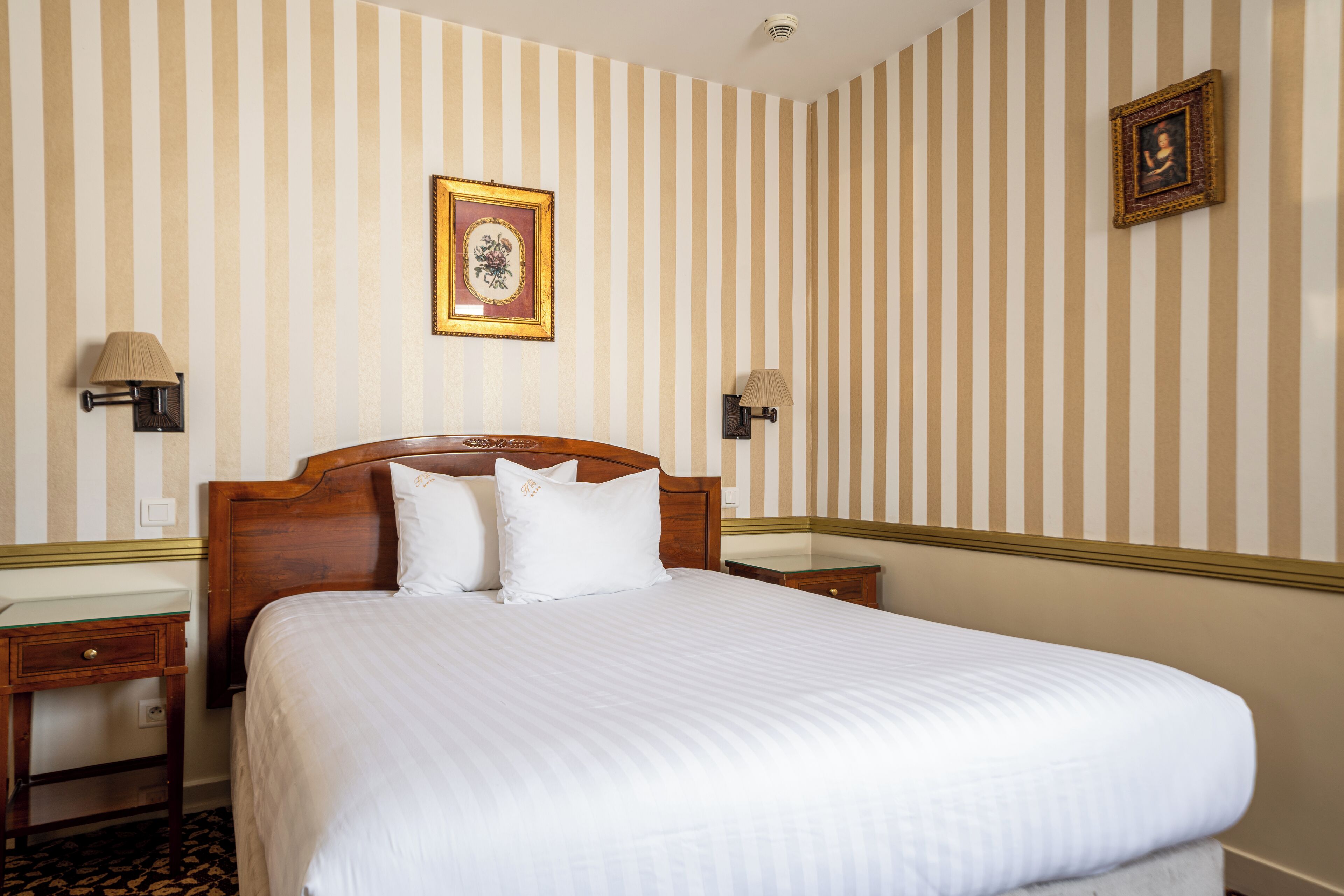 A hotel room with a large bed, two bedside tables, and a wall with striped wallpaper.
