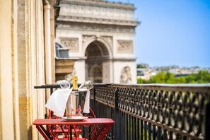 A balcony with a table set for two, a bottle of champagne, and a glass of wine. In the background, the Arc de Triomphe is visible. - Hotel Belfast (Paris)