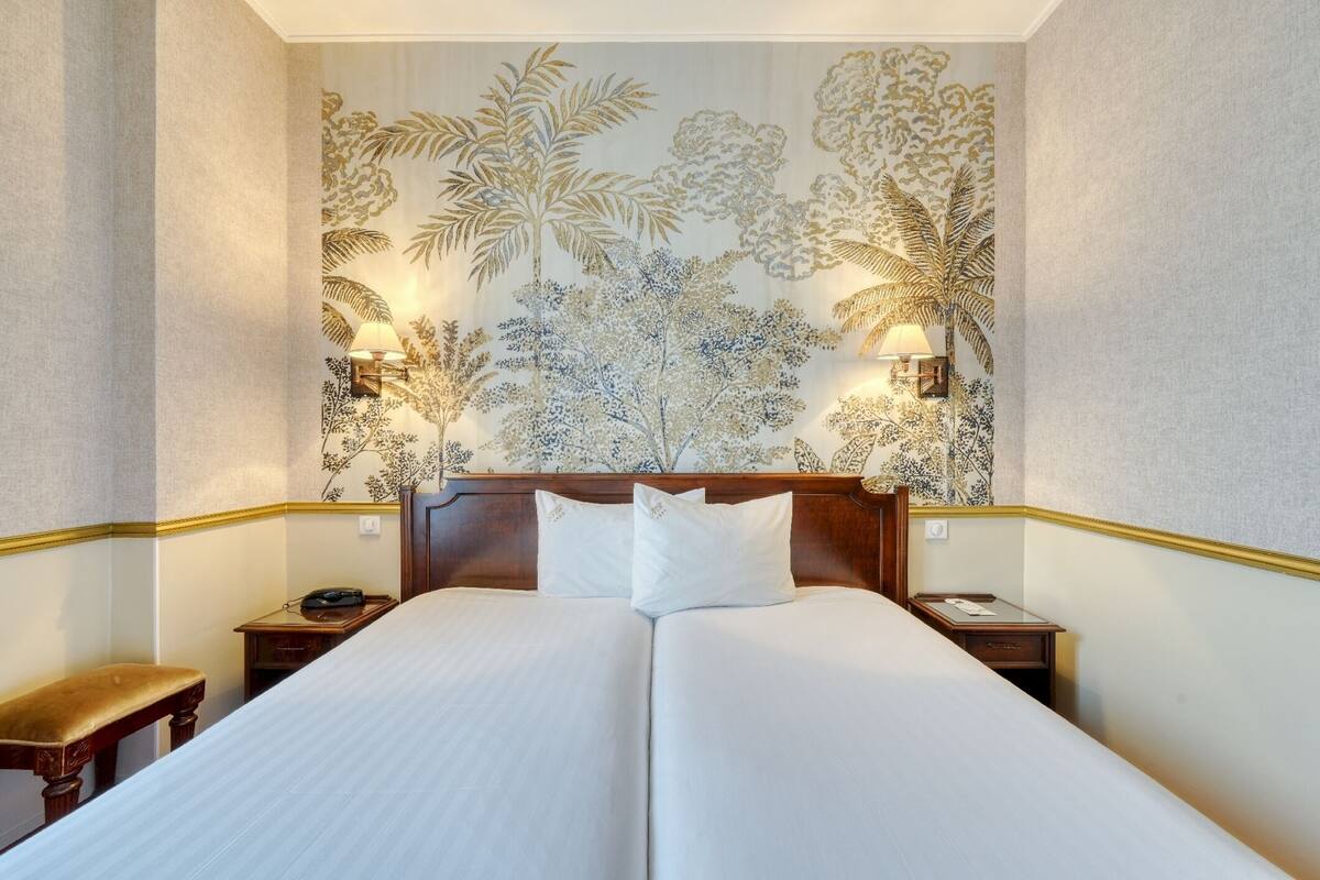 A double bed with white linens, two bedside tables, a wooden headboard, and wall-mounted lamps.