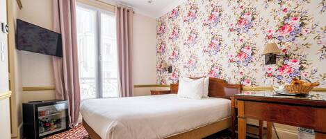 A hotel room with a bed, a desk, a television, and a window with curtains.
