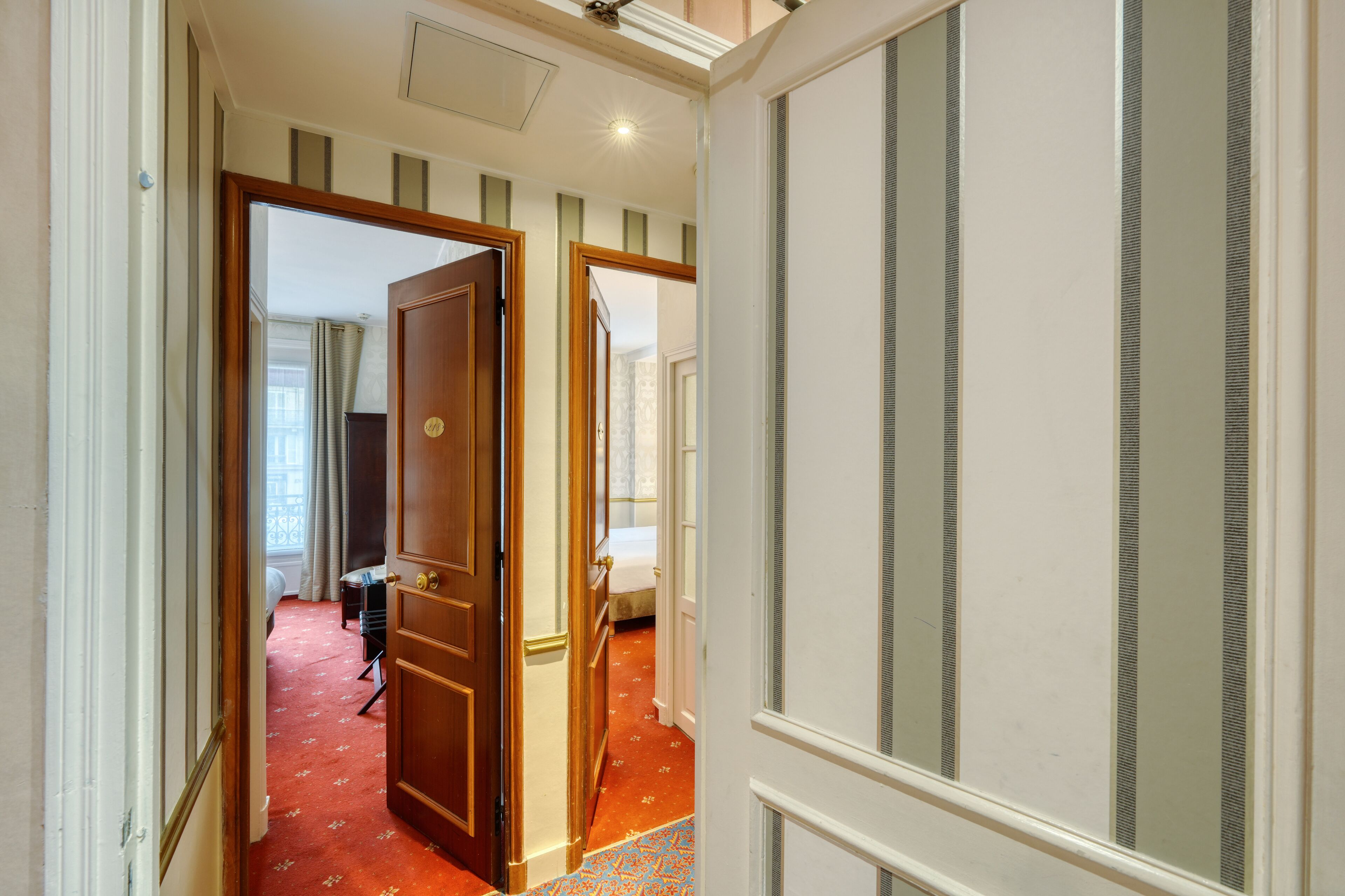 Ein Hotelkorridor mit rotem Teppich, Holztüren und einem Bett im Hintergrund.
