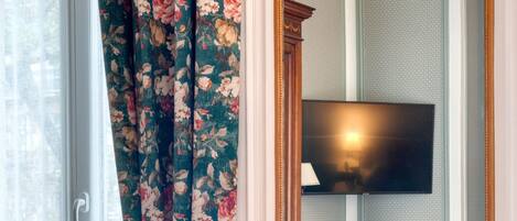 A room with a large window, a sofa, a mirror, and a television.