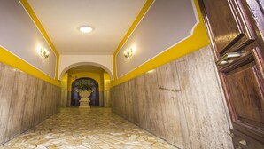 A hallway with a tiled floor, wooden doors, and a central archway leading to a room with a large window. - Hotel Giorgi (Rome)